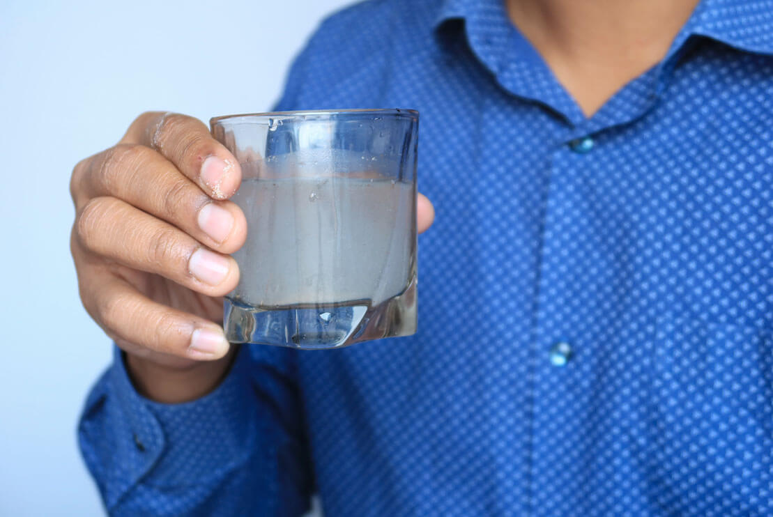 Man holding a glass of unfiltered, murky water.